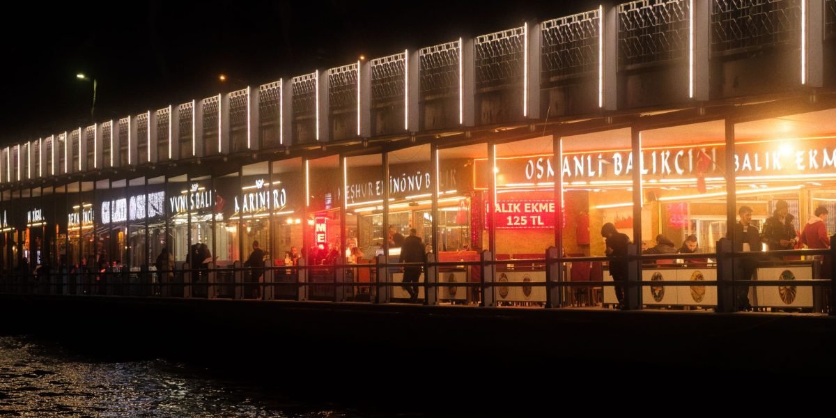 A vibrant scene of people enjoying outdoor dining along a scenic waterfront promenade.